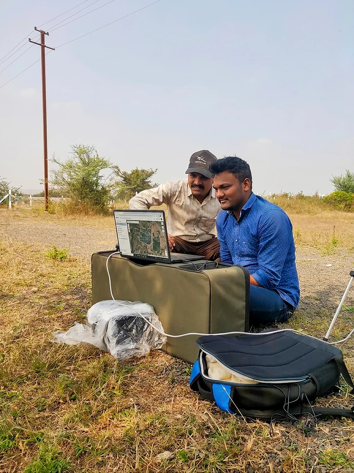Two Schnell engineers reviewing captured multispectral data on a laptop beside their equipment cases in a field