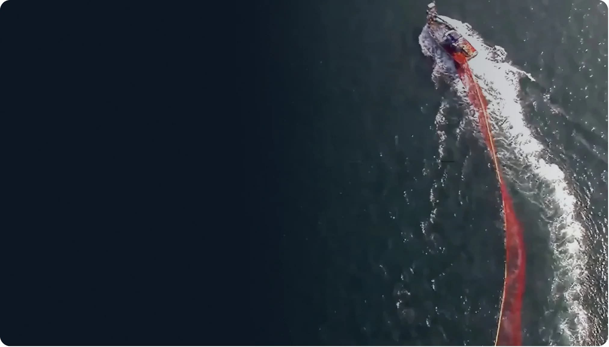 Aerial view of a fishing vessel hauling a long red purse seine net through open sea
