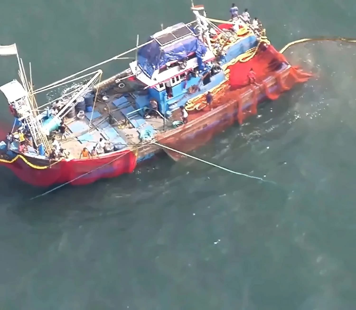 Vessel identification: a trawler with a red purse seine net paid out alongside, crew visible on deck