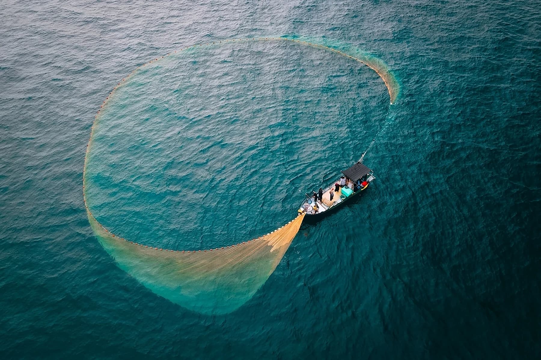 Aerial view of a fishing boat drawing a purse-seine net in a wide circle on open water