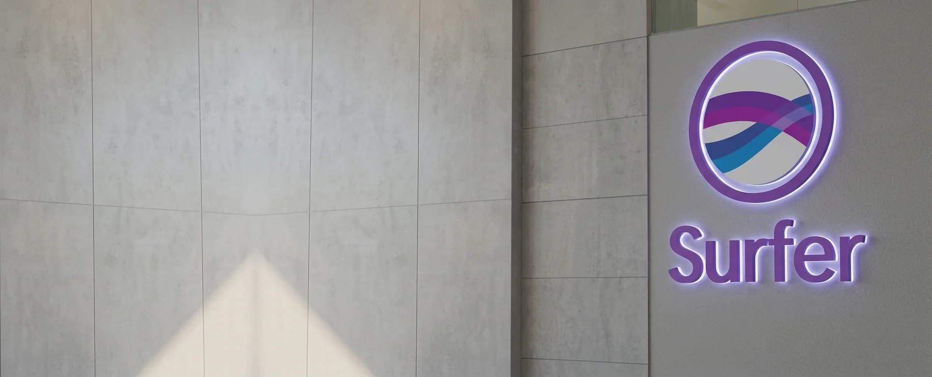 Illuminated Surfer logo sign mounted on a grey concrete wall